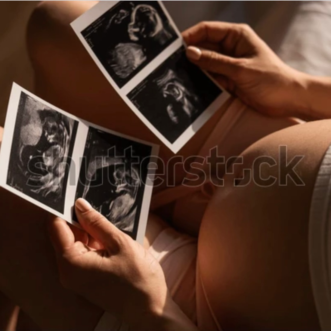 Schwangere Frau sitzt im warmen Licht und betrachtet Ultraschallbilder ihres ungeborenen Babys – Kinderwunsch, Schwangerschaft, Pränatal-Vorsorge.