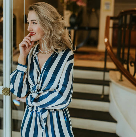 Content Creator in blau weiß gestreiftem Kleid lächelt im eleganten Interieur neben Treppe, Symbolfoto für das Wonder Partnerprogramm für Creator und Influencer.