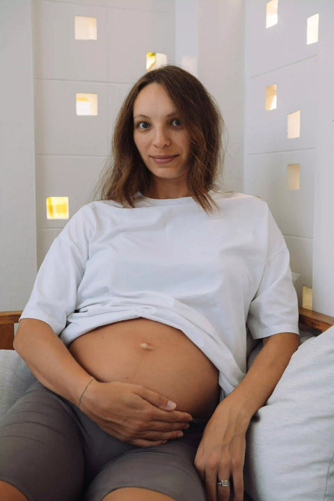 Schwangere Kundin im weißen T Shirt zeigt ihren Babybauch, Kundenfoto zur Rezension des Wonder Schwangerschaft Produkts auf der Produktqualität Seite.