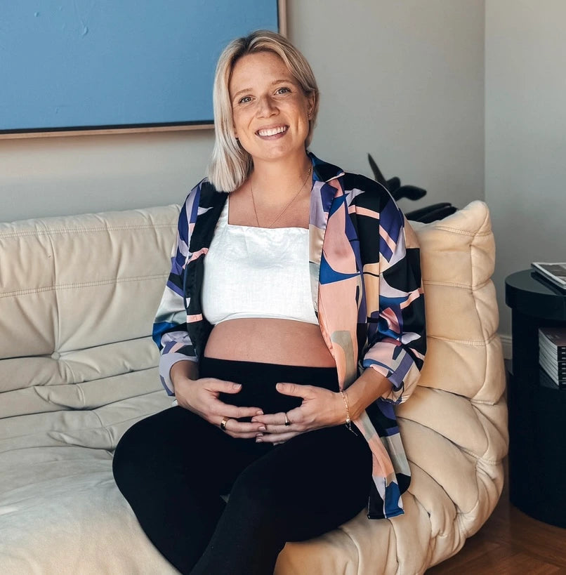 Sonja Hüser, Gründerin von Wonder, sitzt lächelnd und schwanger auf einem Sofa und hält ihren Babybauch
